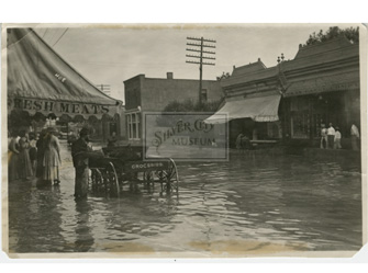 A view of a flood on Bullard Street looking northeast and showing the buildings along the east side of Bullard Street, Silver City, NM. Buildings visible include the James Corbin building and the grocery store of E.M. Young. Circa 1910. From the collection of the Silver City Museum.